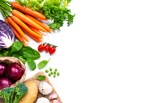 Food backgrounds: overhead view of healthy fresh organic multicolored vegetables arranged at the left border of a white background making a frame and leaving useful copy space for text and/or logo at the right. The composition includes carrots, tomato, spinach, green peas, Spanish onion, lettuce, broccoli, cabbage, potato and garlic. High resolution 42Mp outdoors digital capture taken with SONY A7rII and Zeiss Batis 25mm F2.0 lens