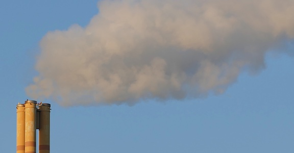 A thick cloud of exhaust rises up from a chimney in the blue sky