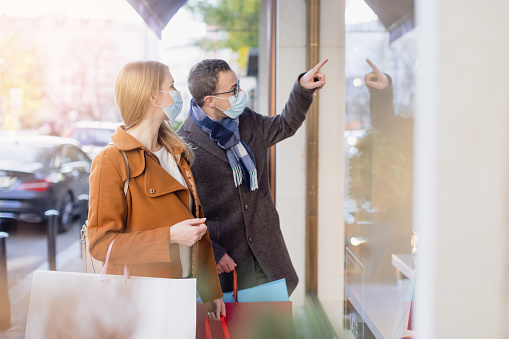 Couple doing shopping during partial lockdown standing in front of shop window with mask