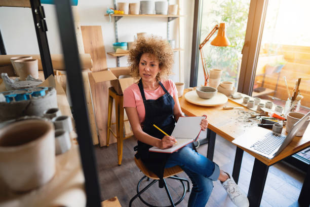 istock Female potter with a planner book and laptop in her pottery studio 1288666998