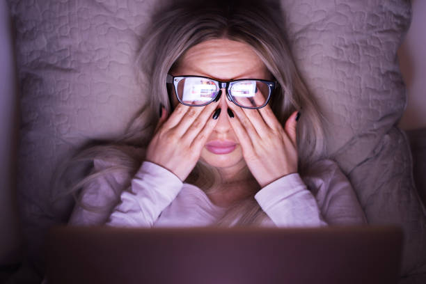 schläfrige frau mit brille, die sich die augen reibt, fühlt sich müde, nachdem sie am laptop gearbeitet hat und auf dem kissen liegt. sich überarbeiten - human eye rubbing tired glasses stock-fotos und bilder