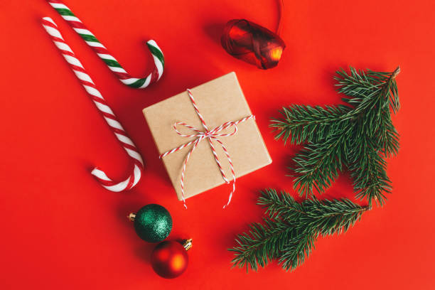 istock Gift box with spruce branches, balls and candy canes on a red background. 1288678412