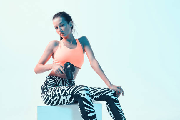 istock Percussion massager, athletic young female massaging leg in neon studio light for effective recovery after workout 1288680752