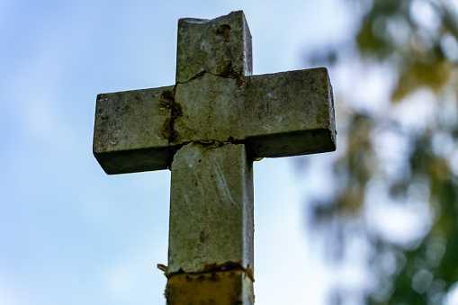 Old and cracked stone cross, a symbol of Christianity, close up with blurred background.