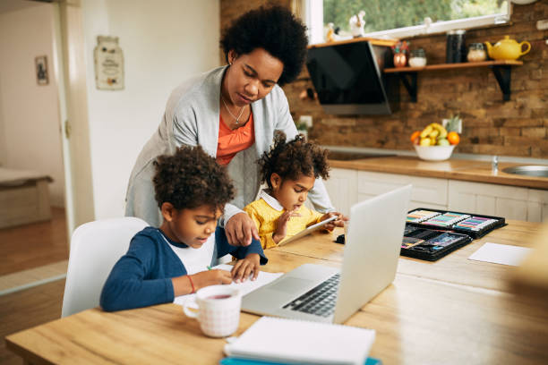 African American mother assisting her kids in learning at home. Black single mother helping her kids with learning at home. Small boy is writing on the paper while girl is using touchpad. homeschooling photos stock pictures, royalty-free photos & images