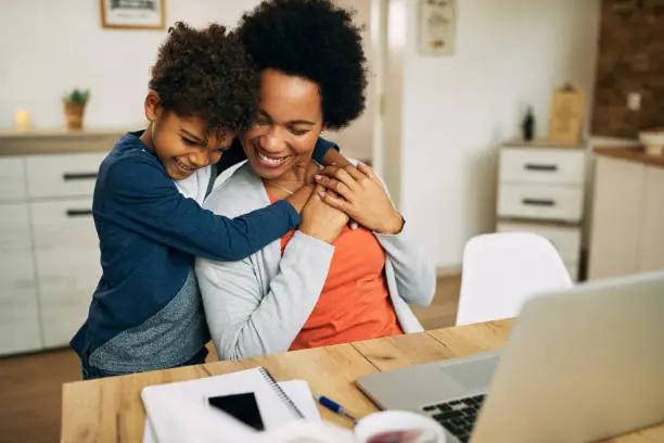 Happy working black mother and her small son embracing at home.