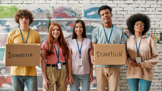 Young diverse volunteer group smiling at camera, holding donation boxes, Happy team working for a charity, donating apparel to needy people, Front view, Web Banner