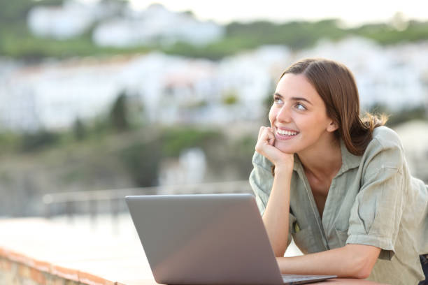 istock Tourist dreaming with a laptop looking at side in a balcony 1288691375