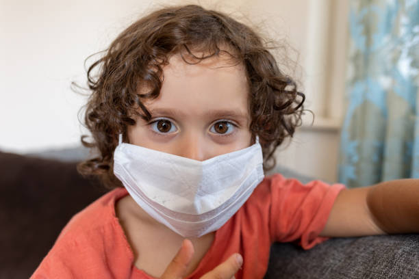istock Boy wearing protective face mask and sitting on sofa at home 1288694111