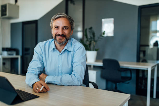 homme avec le visage heureux, travaillant au bureau, tout en regardant l’appareil-photo. - 45 49 ans photos et images de collection