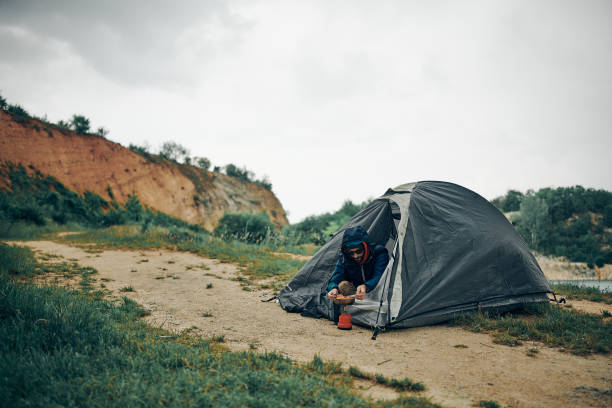 istock Young attractive bearded man sitting next to a tent on a camping trip and preparing lunch. 1288699043