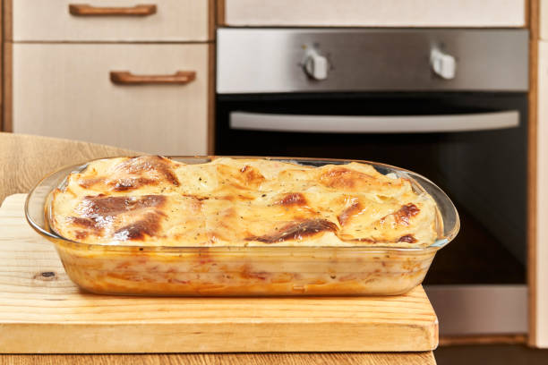 Freshly baked hot lasagna with melted cheese and gratin on a wooden board in a home kitchen stock photo
