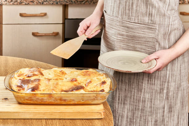 Woman cook serves with a wooden spatula a hot lasagna freshly baked with melted cheese and au gratin in her kitchen