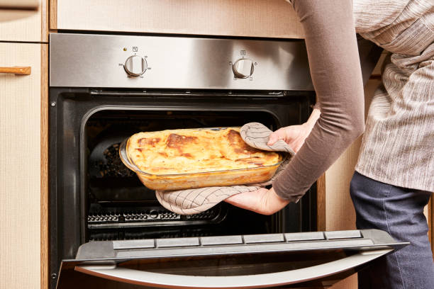 Woman cook takes out a freshly baked lasagna with melted cheese and gratin from the hot oven in her kitchen stock photo