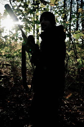 Male sniper armed with rifle equipped with scope and silencer moving quietly through forest