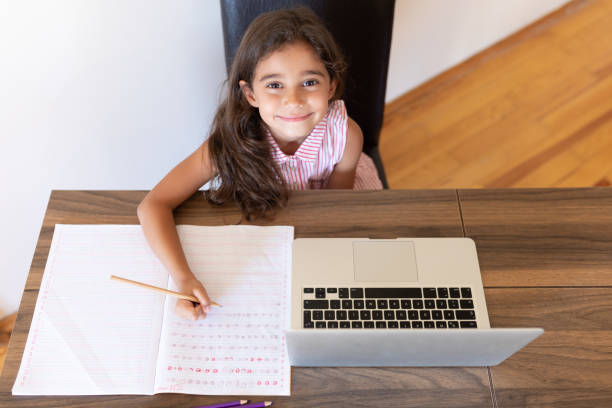 istock Girl doing homework writing in book using laptop at home 1288706082