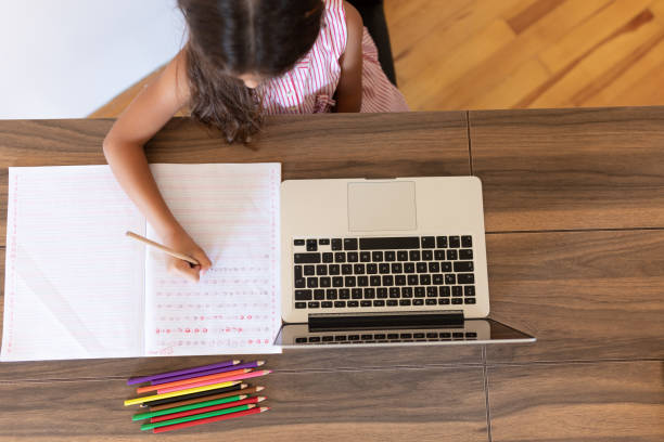 istock Girl doing homework writing in book using laptop at home 1288706163