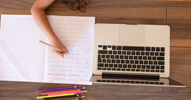 istock Girl doing homework writing in book using laptop at home 1288706186