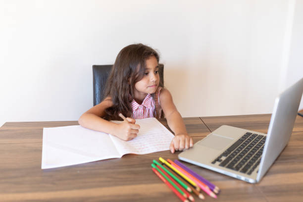 istock Girl doing homework writing in book using laptop at home 1288706198