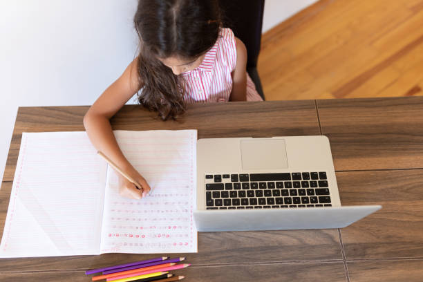 istock Girl doing homework writing in book using laptop at home 1288706221