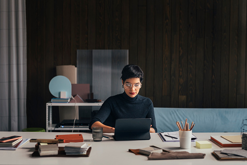 Beautiful mixed race businesswoman in a dark grey outfit using a digital tablet while sitting at her architectural studio.