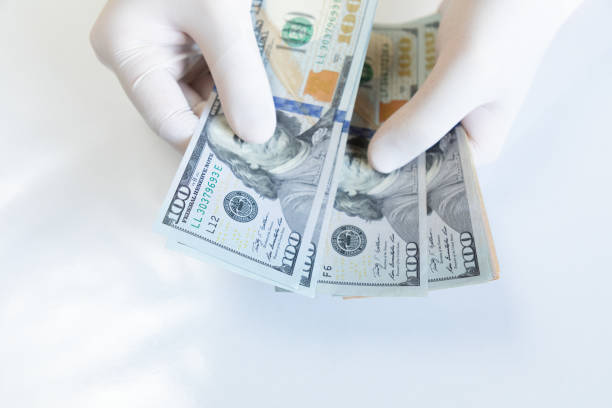 istock Hands wearing protective gloves and counting american dollar bill banknotes 1288720384