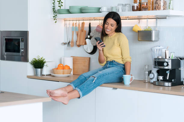 istock Attractive young woman using smart phone while relaxing drinking coffee sitting on the kitchen at home. 1288720922