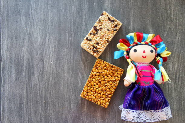 alegrias y palanquetas, mexican amaranth and seed candies with mexican craft doll on vintage wooden gray background the alegrias y palanquetas, mexican amaranth and seed candies with mexican craft doll on vintage wooden gray background candy mexican culture mexican cuisine peanut stock pictures, royalty-free photos & images