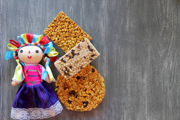 alegrias y palanquetas, mexican amaranth and seed candies with mexican craft doll on vintage wooden gray background the alegrias y palanquetas, mexican amaranth and seed candies with mexican craft doll on vintage wooden gray background candy mexican culture mexican cuisine peanut stock pictures, royalty-free photos & images