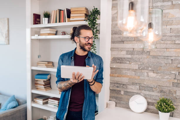 young man turning on a home smart system using digital tablet - portrait tattoo photography color image imagens e fotografias de stock