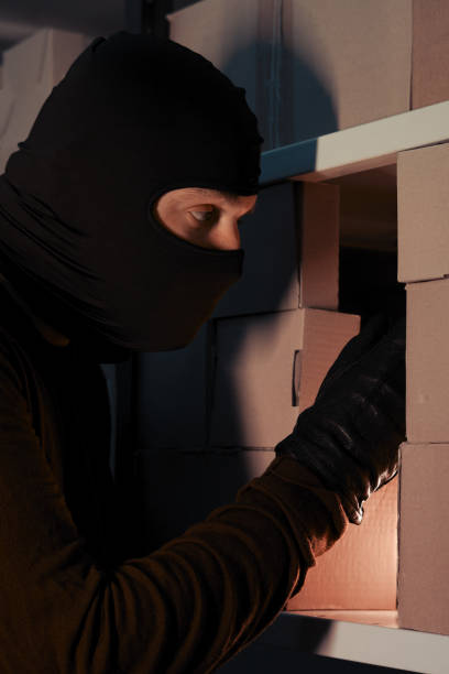 istock Thief in a ski mask steals a parcel in a warehouse in the dark. Concept of security problems in warehouses and stores 1288731687