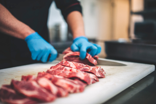 Carnicero masculino cortó carne cruda con cuchillo afilado en la cocina de los restaurantes photo