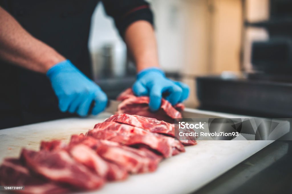 Male butcher cut raw meat with sharp knife in restaurants kitchen closeup view of a young caucasian man cutting raw pork neck with sharp knife. He makes steaks for grill in restaurant kitchen Meat Stock Photo