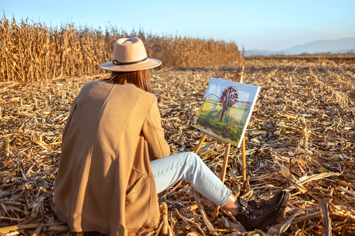 Beautiful young woman painting on canvas in nature in sunset. One woman painter artist. Outdoor