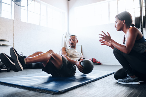 Shot of a man working out with the help of his coach at the gym