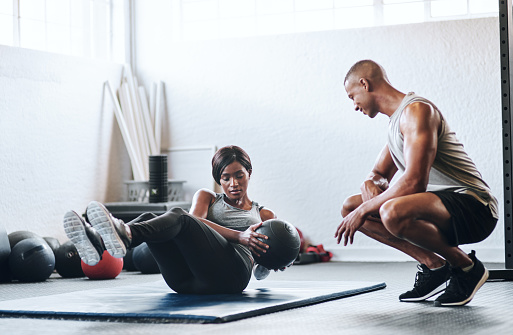 Shot of a woman working out with the help of her coach at the gym