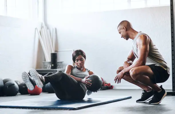 Shot of a woman working out with the help of her coach at the gym