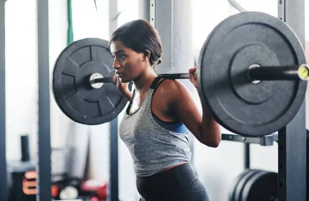 Cropped shot of a young woman working out with a barbell at the gym