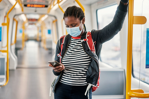 Shot of a young woman wearing a face mask and using a smartphone while traveling on a bus