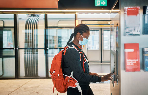 The smartest device for a safety conscious traveller Shot of a masked young woman using a smartphone at a pay station during her commute contactless airport stock pictures, royalty-free photos & images