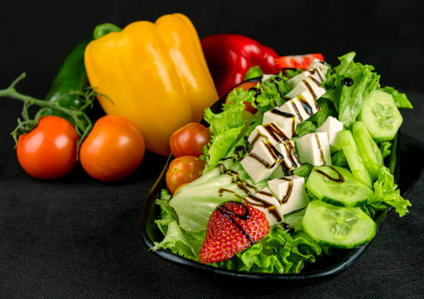 FOOD - Mixed salad with cheese and strawberry on a black background with decorative vegetables. With text area