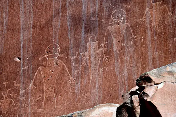 Human-shaped petroglyphs carved (or pecked) into the cliff rock surface by Indians of the Fremont Culture between 300 and 1300 AD. Petroglyph panels throughout the park depict ancient art and stories of these people who lived in the area for about 1000 years. Capitol Reef National Park, Utah, United States. Bullet holes and graffiti left by early tourist visible as well.