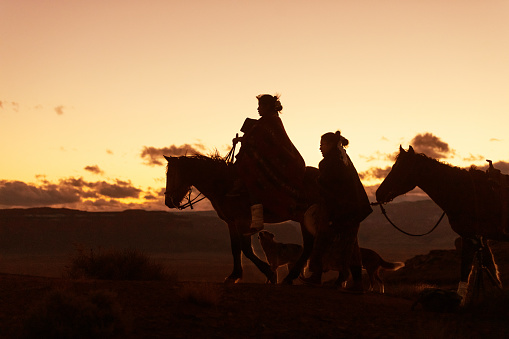 Silhouettes of Navajo family on horses traveling on the Arizona desert - USA