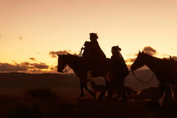 Photo of Silhouettes of Navajo family on horses traveling on the Arizona desert - USA