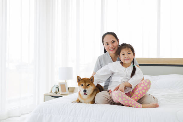 istock Mother and daughter sit on white bed with a dog. 1288745053