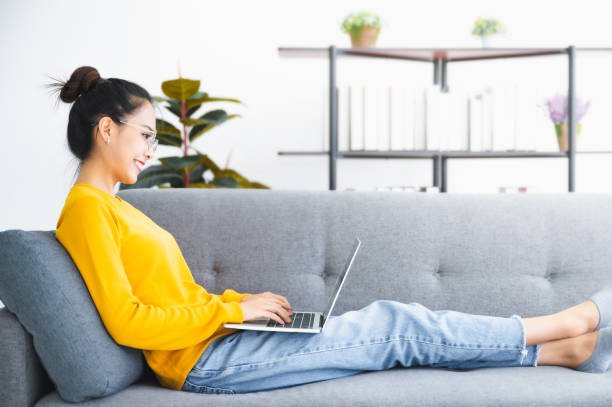 istock Beautiful young asian woman using computer laptop working on sofa in living room 1288745331