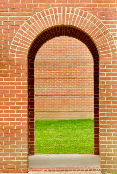 A double arch in a breezeway frames grass and a brick wall in the background. Focus on foreground.