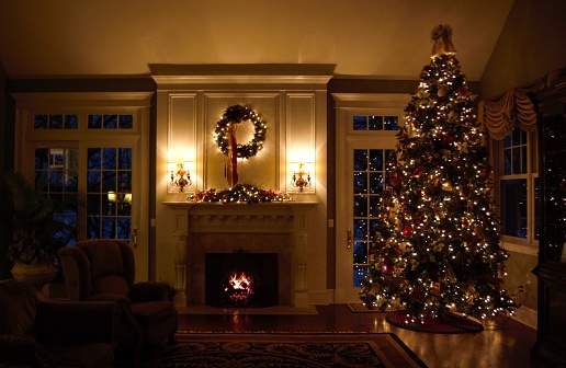 An elegant living room, dimly light, decked out with Christmas decorations and a roaring fire.