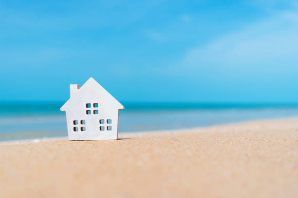 istock Closed up tiny home models on sand with sunlight and beach background. 1288754262