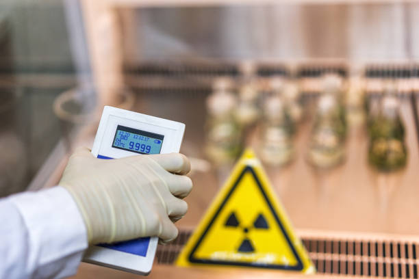 the scientist keeps a dosimeter in his hand to measure the level of radioactive contamination the scientist measures the level of radiation against the background of the sign of radiation hazard with the help of a dosimeter radiation dosimeter stock pictures, royalty-free photos & images